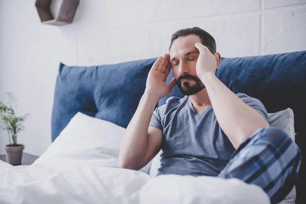 頭痛のベッドの上に座っていると白人の髭の男 — ストック写真