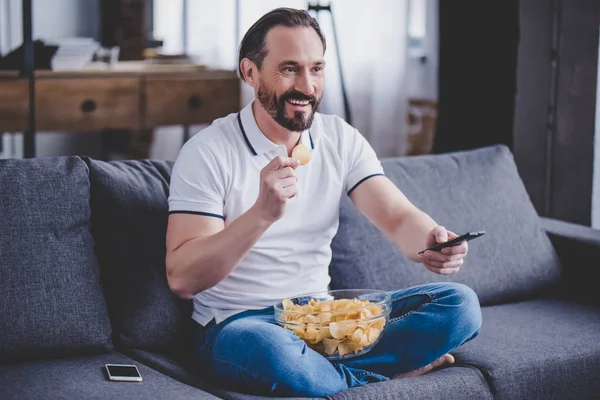 Hombre Barbudo Sonriente Sentado Sofá Viendo Televisión Comiendo Patatas Fritas — Foto de Stock