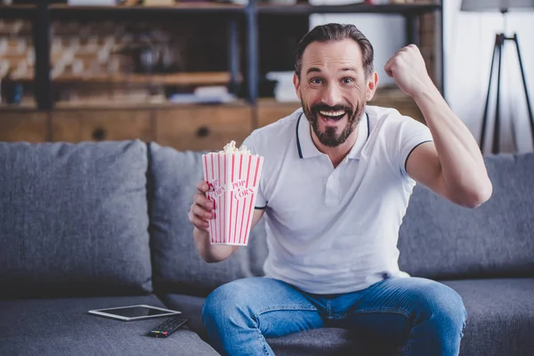 Excited man with popcorn watching tv at home