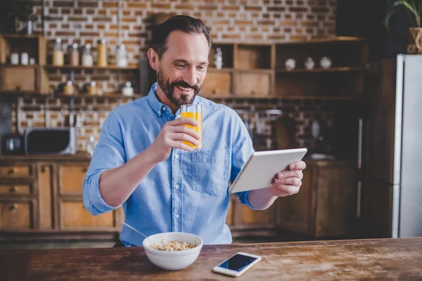 Усміхнений Бородатий Чоловік Тримає Склянку Апельсинового Соку Сніданок Використовує Цифровий — стокове фото