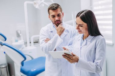 düşünceli doktor ve Yardımcısı modern diş kliniği dijital tablet ekranında bakarak