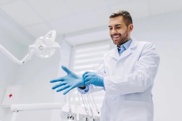 portrait of smiling young male dentist wearing medical gloves in dental clinic