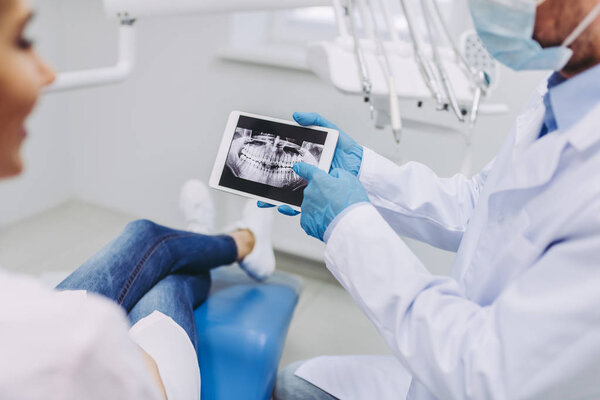 male doctor and female patient looking at digital tablet screen with x-ray in modern dental clinic