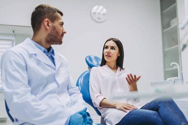 female patient in dental chair and male dentist talking in dental clinic