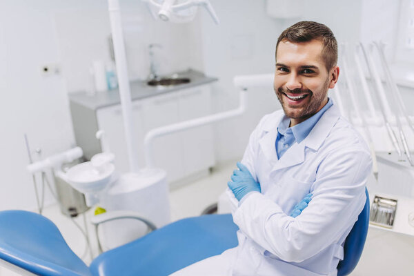 overhead view of smiling male doctor with crossed hands looking at the camera in dental clinic