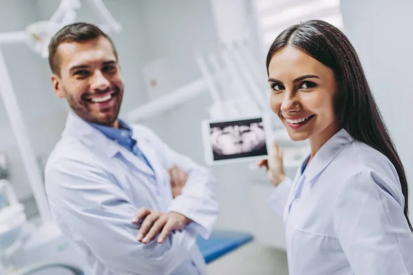 Doktor ve Yardımcısı x-ray modern Diş Kliniği ve looing kamera ile dijital tablet ekranında tutan gülümseyerek