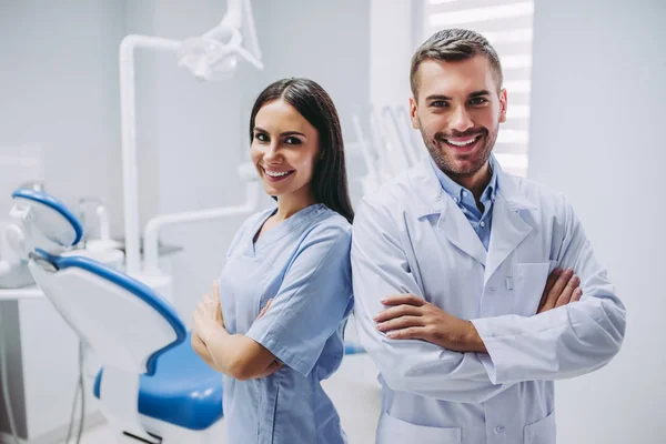 gülümseyen doktor ve Yardımcısı çapraz elle diş kliniği kamera bakıyor