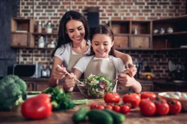 gülümseyen Anne kızı mutfak kase salata savurma yardım