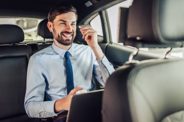 Arabada laptop ve kulaklık kullanarak gülümseyen işadamı portresi