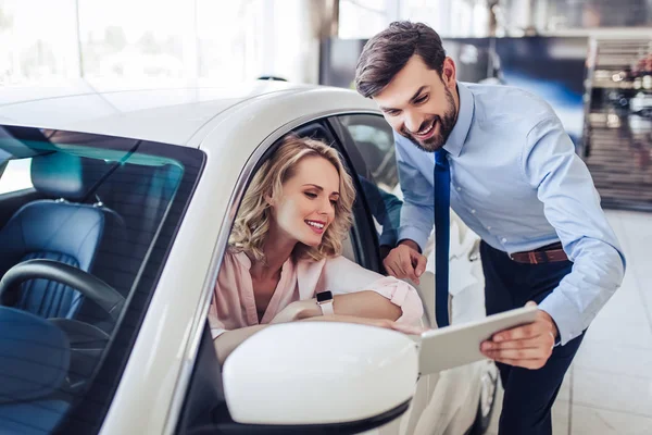 微笑推销员的肖像与女性客户坐在汽车上使用数字平板在经销商沙龙 — 图库照片