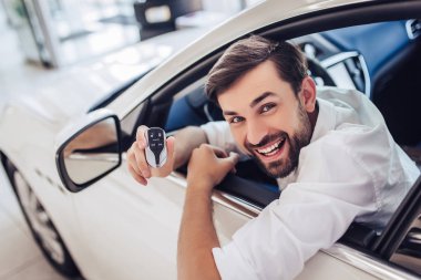 Yeni araba bayilik salonda otururken el hareketi genç mutlu adam portresi