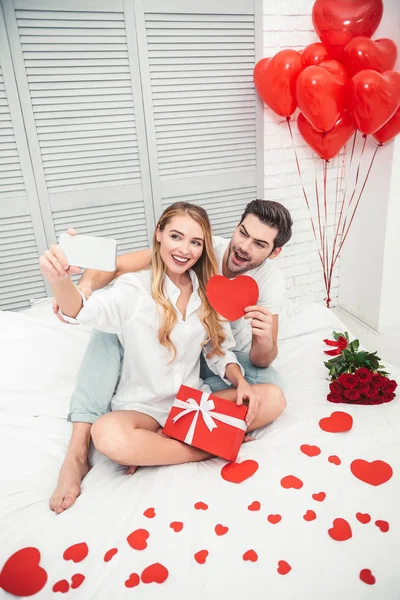 Sorrindo Casal Tirando Selfie Smartphone Com Coração Papel Vermelho Cama — Fotografia de Stock