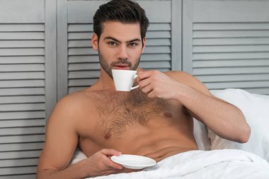 yatakta kahve içme ve kameraya bakarak çıplak yakışıklı adam