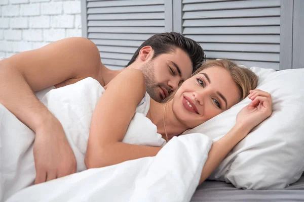 portrait of sleepy man hugging woman looking at the camera in the bed