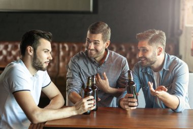 üç arkadaş birlikte kafede bira yudumlarken konuşuyor