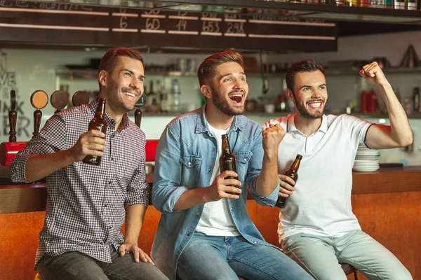 men drinking beer and watching sports game in the bar