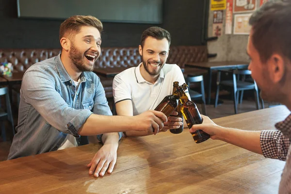laughing friends cheering with beer bottles in cafe