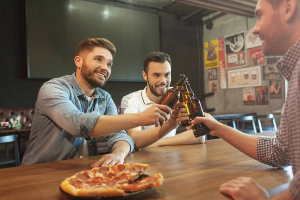 friends cheering with beer bottles and eating pizza in cafe