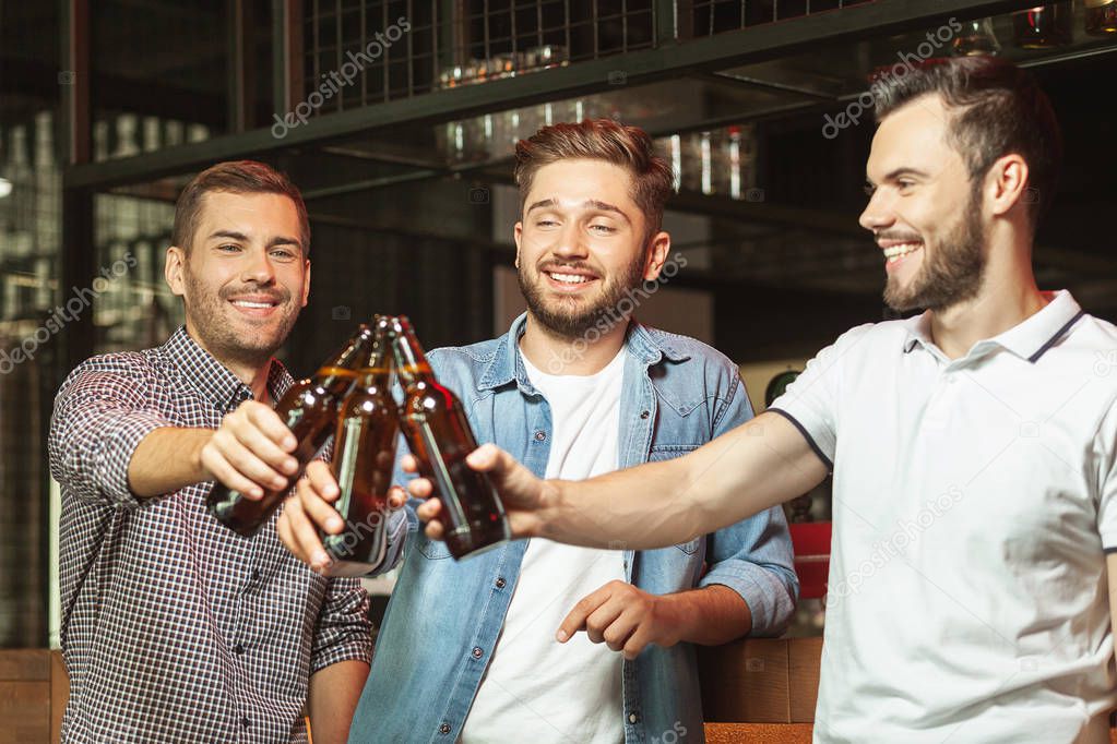 smiling men clicking with beer bottles in the bar