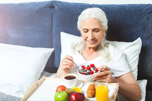 smiling senior woman eating oatmeal for breakfast in the bed