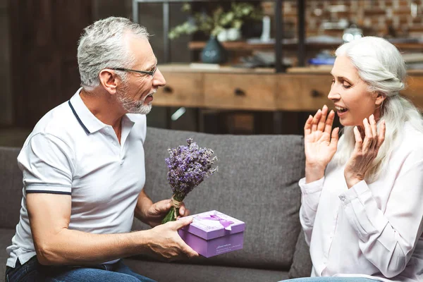 happy surprised woman sitting on the couch with husband giving present