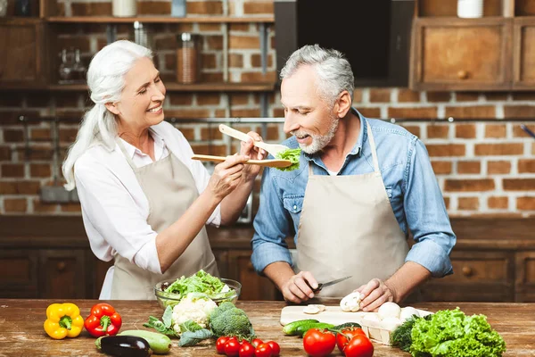 woman feeding man with salad while cooking at the kitchen