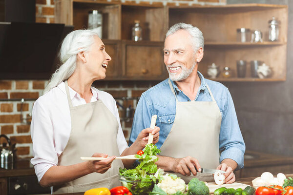 laughing couple looking at each other while preparing food at the kitchen