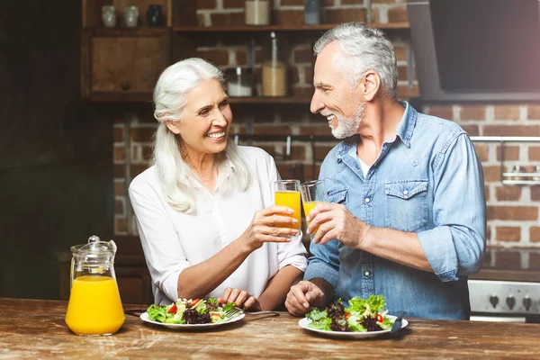 smiling senior woman and man cheering with juice at the kitchen