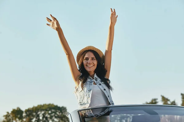 happy young woman raising hands while riding in the cabrio car