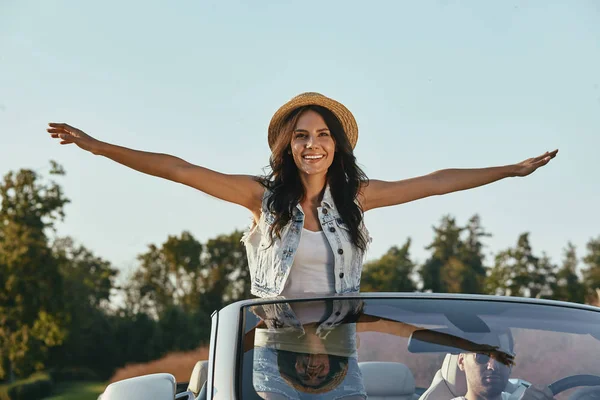 cheerful woman raising hands while man driding cabrio
