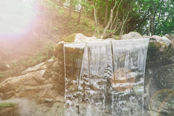 Garden waterfall of stones. Water flows through the stone. The morning sun shines on the waterfall.