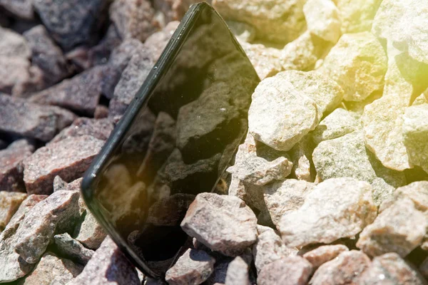 Broken cellphone abandoned and lost among the gravel and sun beam lights