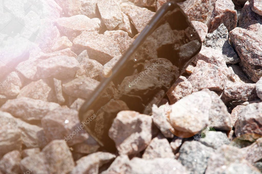 Broken cellphone abandoned and lost among the gravel and sun beam lights