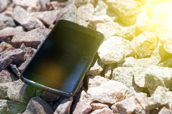 Broken cellphone abandoned and lost among the gravel and sun beam lights