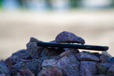 Çakıl taşlarının üzerinde kırık camlar olan cep telefonu, kırılamaz alet.