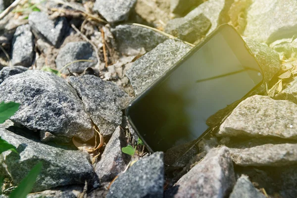 Broken cellphone abandoned and lost among the gravel, with sun beam