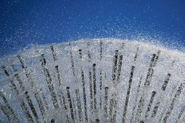 Mavi gökyüzüne karşı güneşin arka ışığında Çeşme. Parkta borudan köpüklü su fışkıran çeşmeler