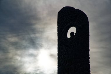 Güneş ve gri gökyüzüne karşı delikleri olan karanlık bir anıt..