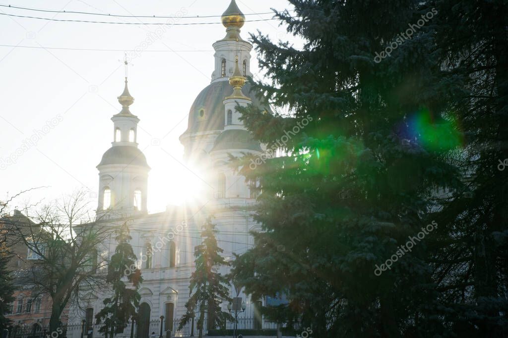 Part of ortodox church in front view with sun behind the clounds. The sun rays breaks through the dome of the church. Cross of church against blue sky