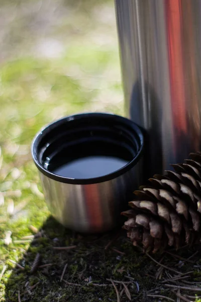 Thermos, cup and pinecone- picnic on mossy rock