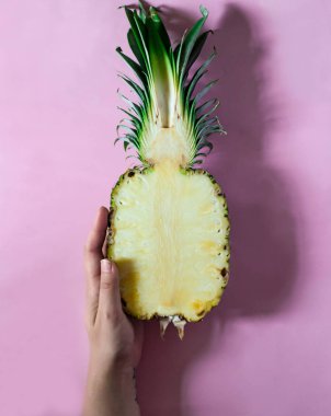 El pembe arka plan üzerinde taze ananas yarısını tutuyor