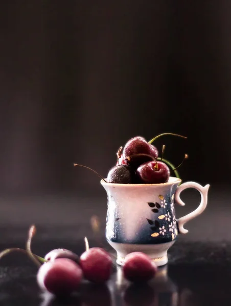 Bodegón oscuro con taza de porcelana de cerezas frescas — Foto de Stock