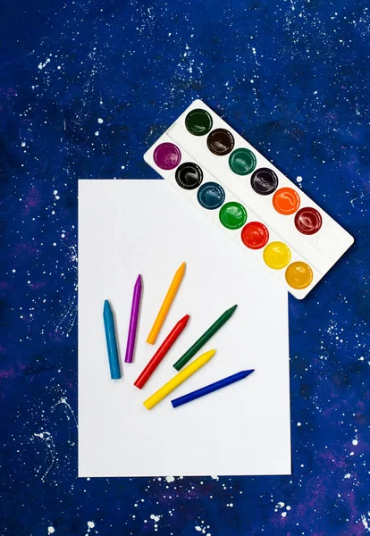 Akvarell paletta többszínű zsírkrétákkal üres fehér papírlapon és helységkék háttérrel — Stock Fotó