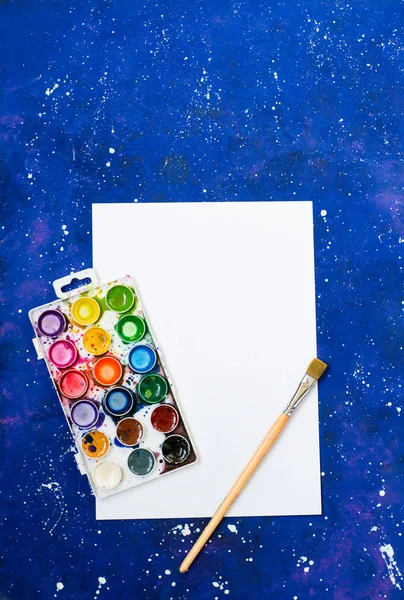 Akvarell paletta és ecset üres fehér lap és kék-tér háttér — Stock Fotó
