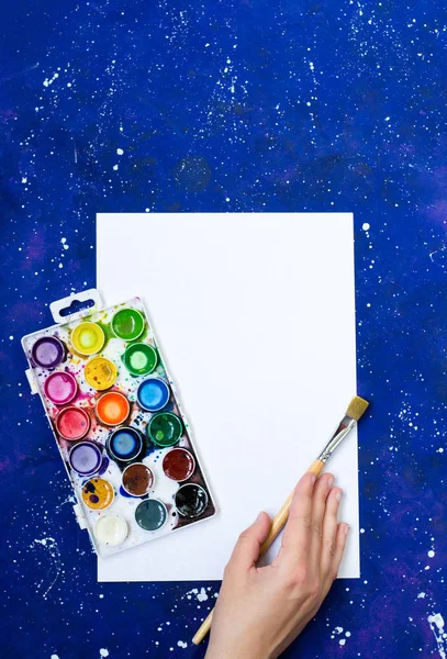 Akvarell paletta és kéz ecsettel üres fehér lap és kék-tér háttér — Stock Fotó