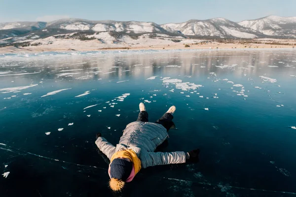 Flicka ligger på ytan transparent isen och ser på himlen och en åtnjuter semester och bra väder. Hon ser på molnen och tänker om hur vacker natur i Sibirien — Stockfoto