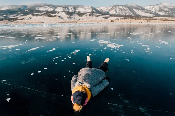 Ragazza si trova sulla superficie ghiaccio trasparente e guarda nel cielo e si gode di vacanze e bel tempo. guarda le nuvole e pensa a quanto sia bella la natura della Siberia — Foto Stock