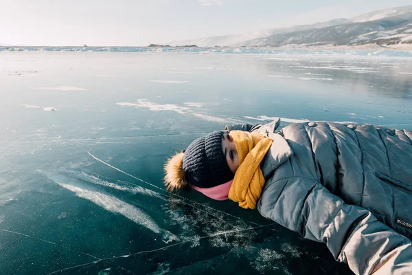 Flicka ligger på ytan transparent isen och ser på himlen och en åtnjuter semester och bra väder. Hon ser på molnen och tänker om hur vacker natur i Sibirien — Stockfoto