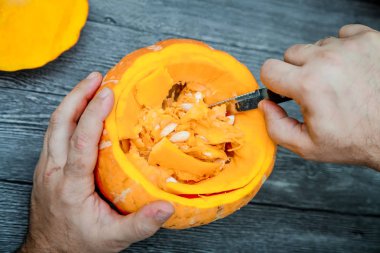 Cadılar Bayramı için kabak maske oyma işlemi. Erkekler elinde bir bıçakla bir Turuncu kabak çekirdeği almak.