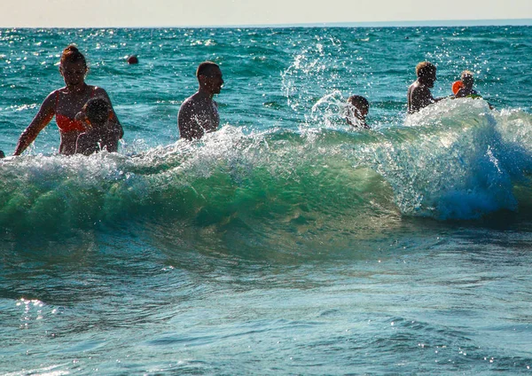 Tormenta en el mar. Una gran ola cierra bañar a la gente. La gente disfruta de las olas y salpicaduras . — Foto de Stock